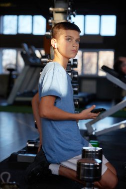 Ciddi bir genç, spor aktivitesi için internetten video eğitimi alırken spor salonunda vücut geliştirme ve vücut çalışmalarına hazırlanıyor.