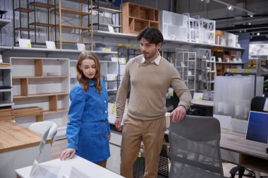 Bir çift, çağdaş bir perakende satış alanında çeşitli şık ofis mobilyası seçeneklerini aktif olarak inceliyor.