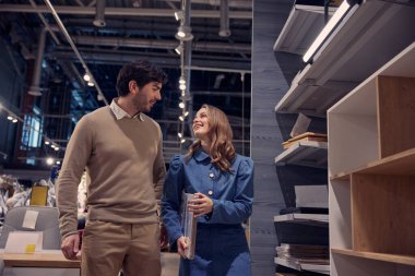 Sevgi dolu çift, şık bir ev eşyaları mağazasında canlı sohbetler yaparken mobilya seçeneklerini araştırıyor.