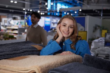 Neşeli ve mutlu bir kadın, rahat bir perakende satış ortamında çeşitli yumuşak havlular arasında neşe içinde poz verir.