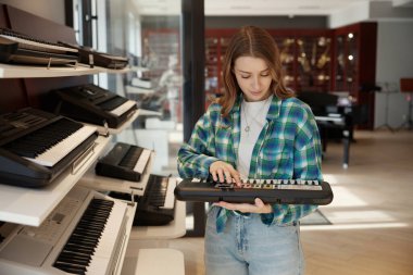 Genç bir kadın, yaratıcılıkla dolu modern bir müzik stüdyosunda neşe içinde zarif bir klavye sergiliyor.