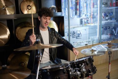 Şık bir ceket giyen bir adam enerjik bir şekilde davul çalıyor ve etrafındaki herkesi ritmiyle büyülüyor.