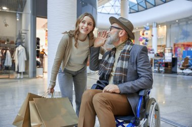 Tekerlekli sandalyedeki bir erkek alışveriş merkezinde birlikte gezinirken bir kadından yardım alıyor.