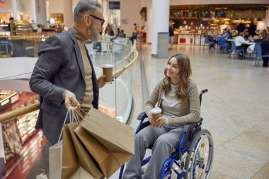 Tekerlekli sandalyedeki engelli genç bayan. Alışveriş merkezinde yaşlı bir adamın yardımıyla.