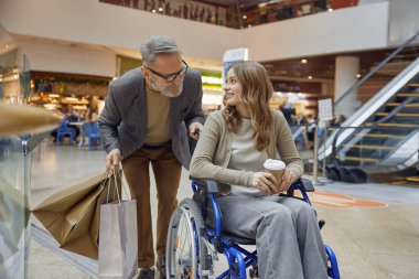 Tekerlekli sandalyedeki bir erkek ve kadın arasında hareketli bir alışveriş merkezinde güzel ve neşeli bir etkileşim başlar.