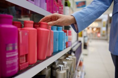 Bir kadın zarif bir şekilde alışveriş yaparken bir perakende mağazasının üst rafında duran bir şişe şampuana uzanıyor.