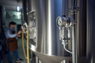 Man dressed in apron is diligently working in brewery, surrounded by various machinery and equipment essential for beer production