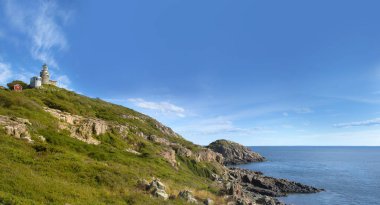 Bir tepenin tepesinde bir deniz feneri, mavi gökyüzünde baltık denizine ve beyaz bulutlara bakıyor.