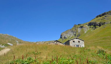  Çayırlarda, arka planda mavi gökyüzünün altında dağ olan eski bir koyun ağılı.