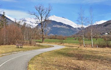 Yeşil kıvrımlı asfalt şeridi karlı dağ arka planına sahip bir dağ vadisini geçiyor. 