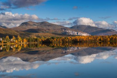Güzel dağlık arazi gökyüzünde bulutlarla birlikte suyu yansıtıyor. 