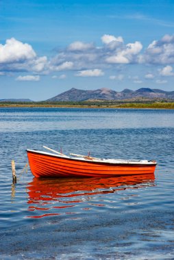 Sardinya 'da denize demirlemiş güzel kırmızı bir tekne. Arka planda mavi gökyüzünün altında dağ var.