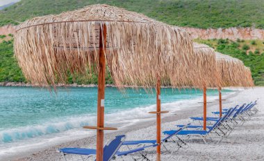 Peloponnese Yunanistan 'daki beyaz çakıl taşı plajında saman şemsiyesi ve güneş şezlongları
