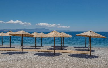 Yunanistan, Moreloponese 'de beyaz çakıl taşlarından oluşan bir plajda saman şemsiyesi.