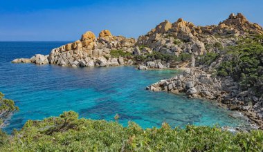 Sardunya 'daki Santa Teresa Gallura' da kayalıklarla ve yeşil bitkilerle çevrili kristal anturkuaz deniz manzarası.