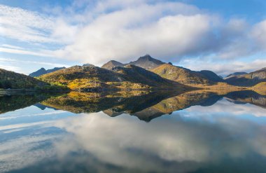Norveç 'in su yüzeyine yansıyan bulutlu gökyüzü altında dağlı güzel manzaralı bir yer..