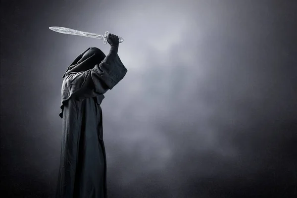 Dark knight with hooded cape and medieval sword over dark misty background