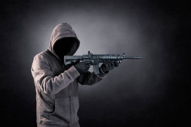 Siyah sisli arka planda saldırı tüfeği olan kapüşonlu bir adam.