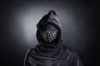 Kapüşonlu, çivili pelerinli, gece karanlığında sisli arka plan maskeli korkunç bir şahıs.