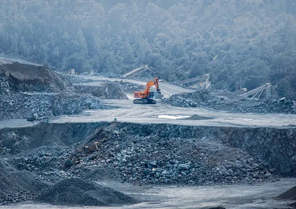 Kazı makinesi, arka planda taşıma bantları ve ormanla birlikte bir veritabanı ocağında çalışıyor. Parekklisia taş ocağı, Kıbrıs