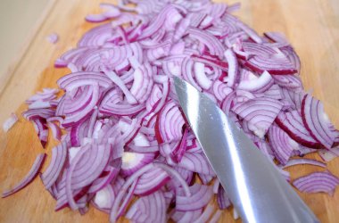 Keskin bir bıçakla tahta kesme tahtasının üzerinde kırmızı soğan dilimlemek. 