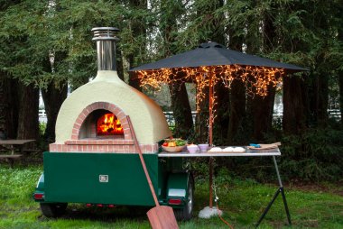 Ateşli pizza fırını, yemek masası ve dekoratif gece lambaları..