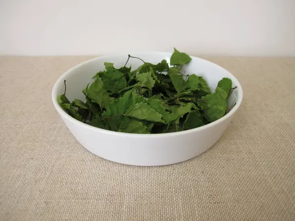 Porselen bir kasede kurumuş huş yaprağı ve bitki çayı.