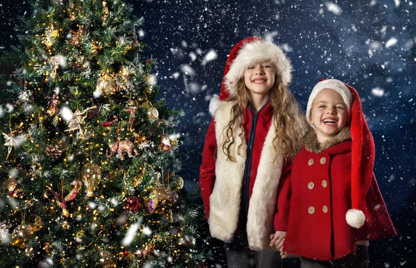 圣诞节的孩子们就在圣诞树旁边 圣塔哈特快乐的孩子们在享受降雪 用白雪在深蓝色天空的背景上微笑的小女孩 冬季及新年假期 — 图库照片