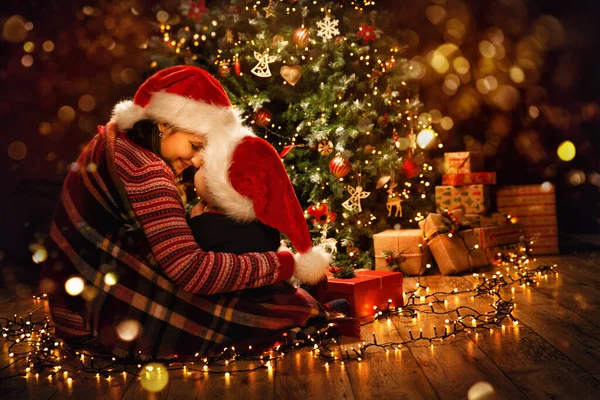 圣诞家庭 在圣诞树旁的圣诞老人小屋 母亲抱着孩子 在黑暗的家房间里装饰着圣诞装饰品 圣诞节庆祝活动和礼物准备 — 图库照片