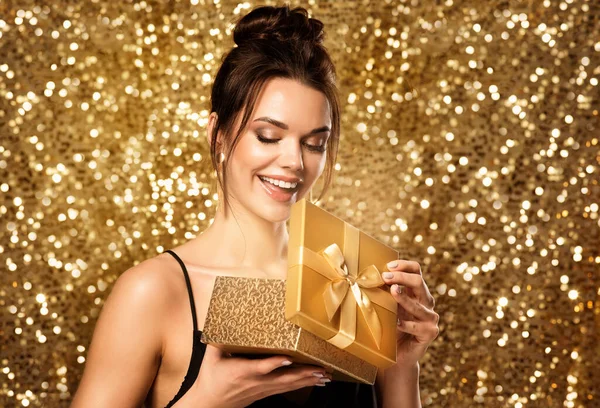 ギフトボックスを開く女性 ゴールド グリッターを背景にゴールデン プレゼントを持つハッピー ガール 美容モデルはクリスマス休暇に驚きを取得します 自然なメイクで笑顔の女性の顔 — ストック写真