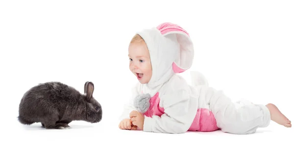 白の上にウサギペットとウサギの衣装で赤ちゃん 幸せな笑顔子供でクリスマススーツ見ますダークグレー毛皮のウサギ横に白い床のプロフィール側のビュー — ストック写真