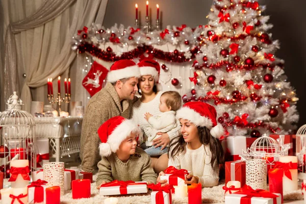 圣诞家庭开幕礼物 有孩子的家庭在圣诞帽旁边的圣诞树与白色礼品盒 圣诞礼物和红色装饰品的室内装修 — 图库照片