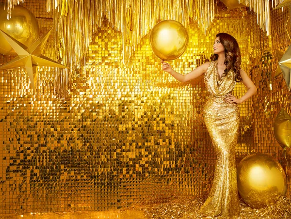 Woman in Golden Sequin Party Dress. Fashion Model in Evening Long Gown over Gold Glitter Wall Interior. Stylish Girl Holding Yellow Foil Balloon celebrate Birthday Holiday