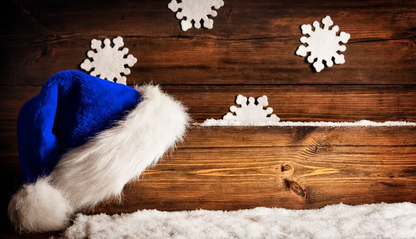 圣诞圣帽挂在木板招牌上 蓝色的圣诞帽盖在褐色的松木背景上 上面有雪花和雪花 圣诞假期装饰概念 — 图库照片