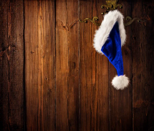 圣诞圣诞圣帽挂在树篱上的木制董事会背景 蓝色的圣诞帽盖过棕色的松木木板墙 圣诞假期概念 — 图库照片