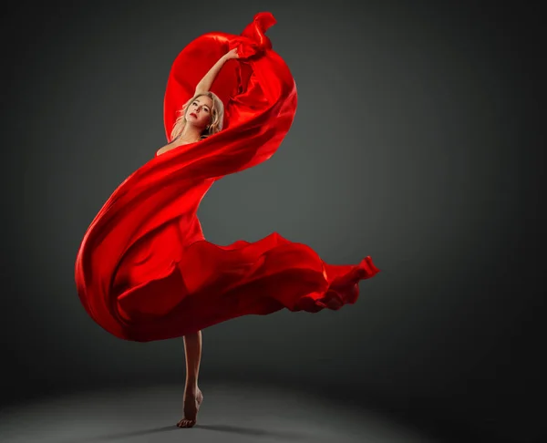風に乗って飛んで赤いシルクファブリックとバレリーナダンス モダンバレエダンサーがダークスタジオの背景を飛び越える 赤いドレスのファッション女性はスカーフを振って包まれた — ストック写真