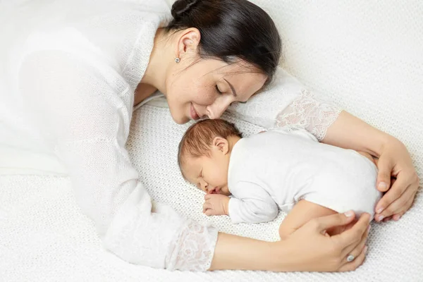 Smiling Mother sleep with Newborn on White Blanket. Dreaming Mom hugging Baby lying down on Stomach. Happy Motherhood and Parenting. Infant Health Care. Child Protection