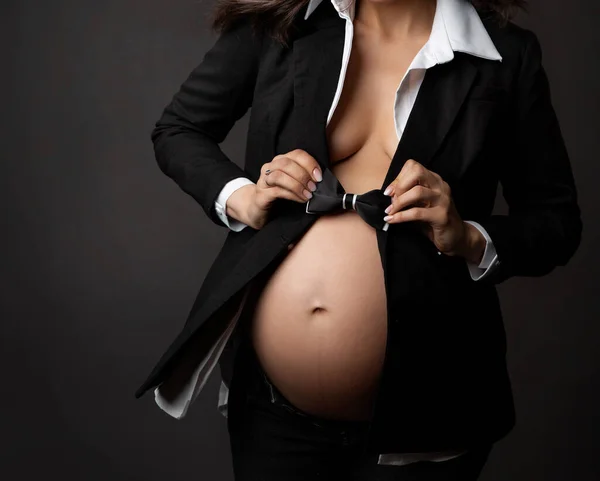 黒い弓で妊娠中の女性腹の閉じるダークグレーの背景にタイ 古典的なビジネススーツでエレガントな未来のお母さん待っている赤ちゃんの男の子 妊娠ファッションスタイル 性同一性概念 — ストック写真