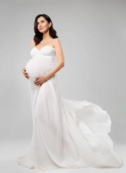 白いロングドレスの妊婦風を見上げて飛んでいます 美しい母のシルクの灰色の背景にガウンを振って夢を見る 妊娠中のファッション服 — ストック写真