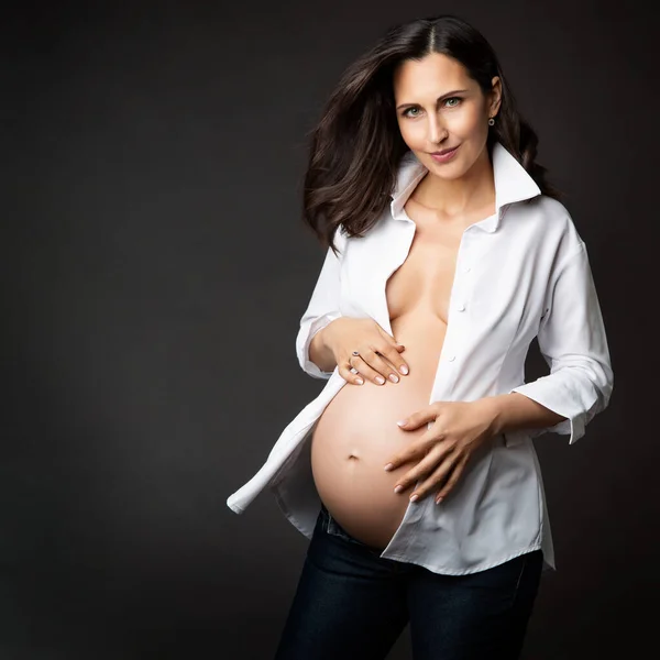 白衬衫而不是黑色背景的快乐孕妇 怀孕时尚与产妇保健护肤 多姿多彩的母亲穿着解开纽扣的衬衫 抱着阿卜杜拉米 — 图库照片
