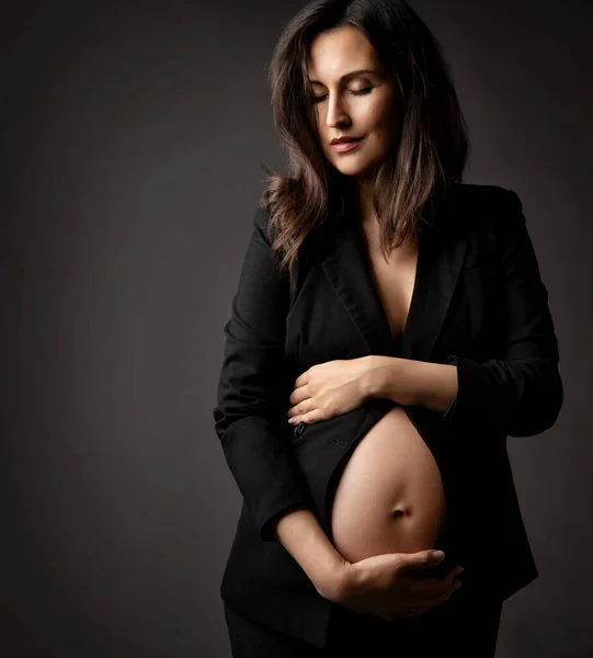 深灰色背景下黑色西装风格的怀孕妇女肖像 怀孕时尚与产妇保健 美丽的妈妈抱着赤身露体的美女低头看 — 图库照片