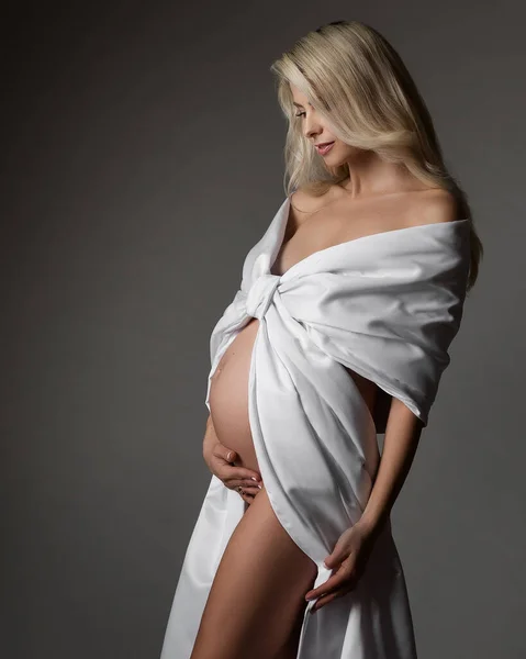 ベリーサイドビューを見て白いドレスの妊婦肖像画 ダークグレーの背景に輝くシルクの美しい母 妊娠中のファッション — ストック写真