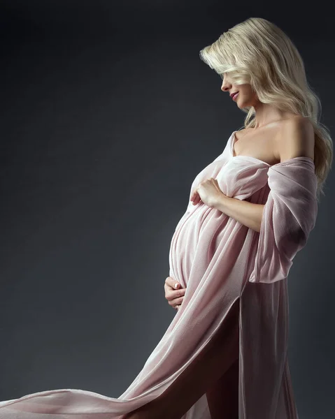 美丽的怀孕妇女看着Belly侧景 在深灰色的粉红衣服中拥抱阿卜杜吉祥的快乐母亲形象 — 图库照片