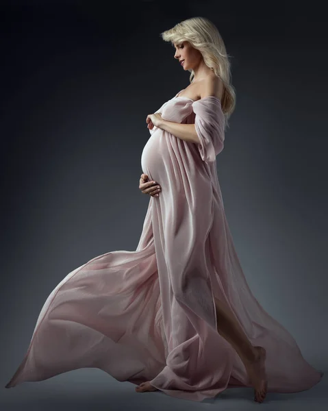 美しい妊娠中の女性は 波のドレスサイドビューで腹を見て Happy Motherプロフィール肖像画受け入れます腹部ピンクゴーン上のダークグレー — ストック写真