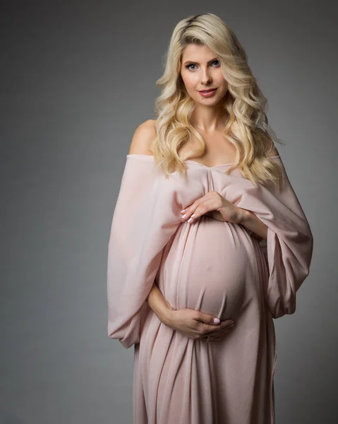 ピンクのシフォンの美しい妊婦の肖像は灰色の上にドレスアップ シルクガウンにカーリーロングヘア メイクで幸せな母 妊娠中のブライダルファッション — ストック写真