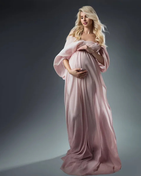 ピンクの妊娠中の女性はダークグレーの背景にドレスを振って チャフォン ガウンの美しい母親はベリーを見ている 妊娠中の肖像画 — ストック写真