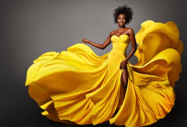 Sarı İpek Elbiseli Moda Kadını Rüzgarda akıyor. Gri üzerinde uzun fantezi elbisesiyle Afro saç stili olan koyu tenli bir model. Mutlu Şık Kız Dansı