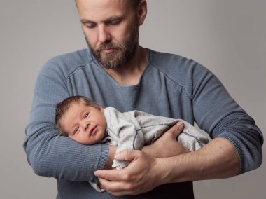 Baba kucağında bebek var. Gri Arkaplan 'da yeni doğmuş bir adam. Acımasız Baba küçük oğlunu sallıyor. Çocuk Geliştirme. Babalar Günü.