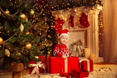 Noel ağacının altındaki Kırmızı Hediye Kutusu 'nun içindeki Noel Çocuğu. Noel Baba Şapkalı Şirin Bebek, Ateş Ağacı ve Şömineli Samimi Oda 'da Sunar