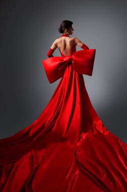 Kırmızı İpek Sırtsız Elbiseli Moda Kadını. Gri Arkaplan Üzerinde Açık Sırt Maxi Elbisesi Giyen Zarif Kadın. Uzun İpek Tren Kumaşlı Akşam Elbisesi Güzel Modeli